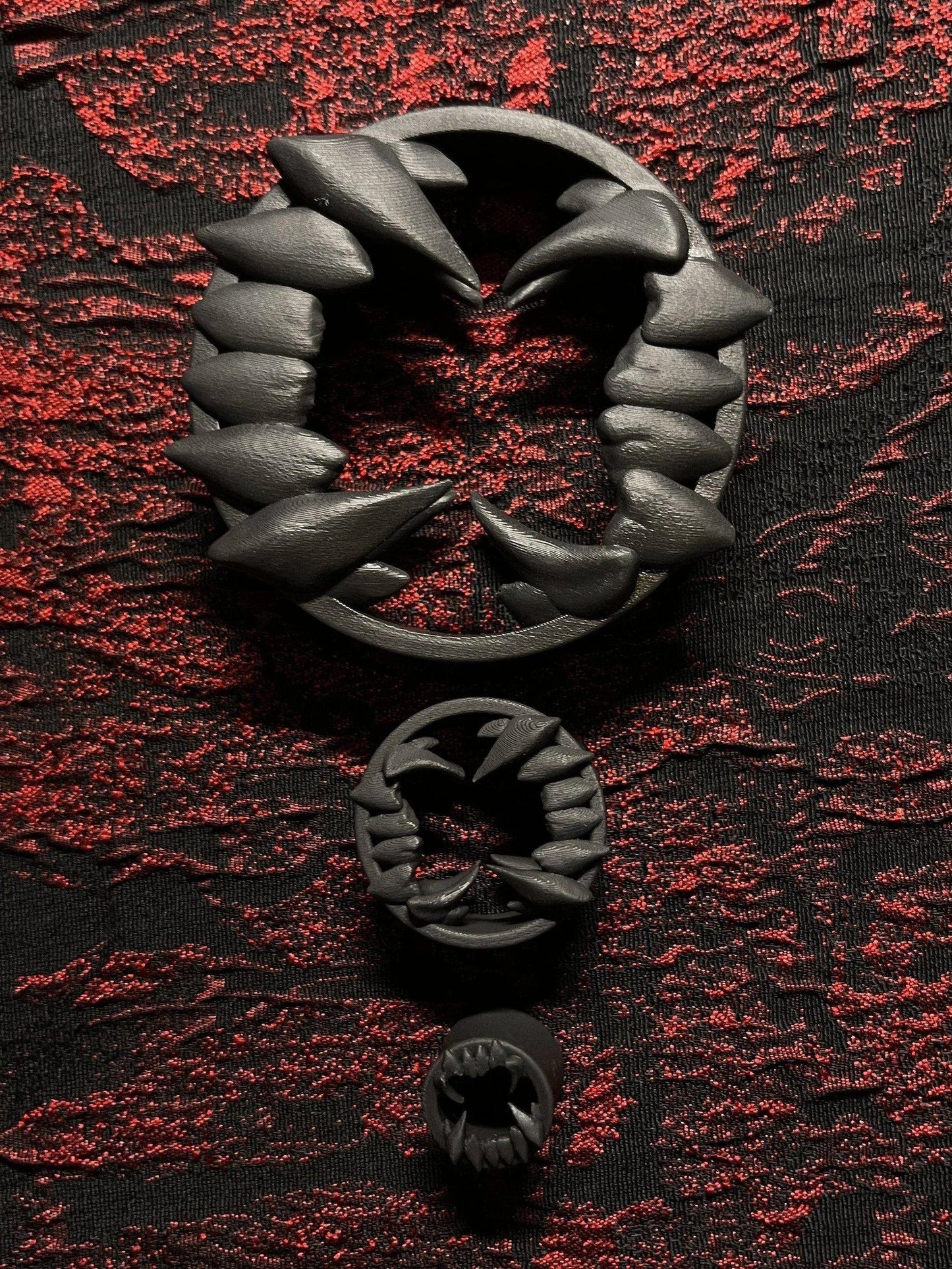Three Beast double flared ear tunnels in different sizes on a red and black textured background