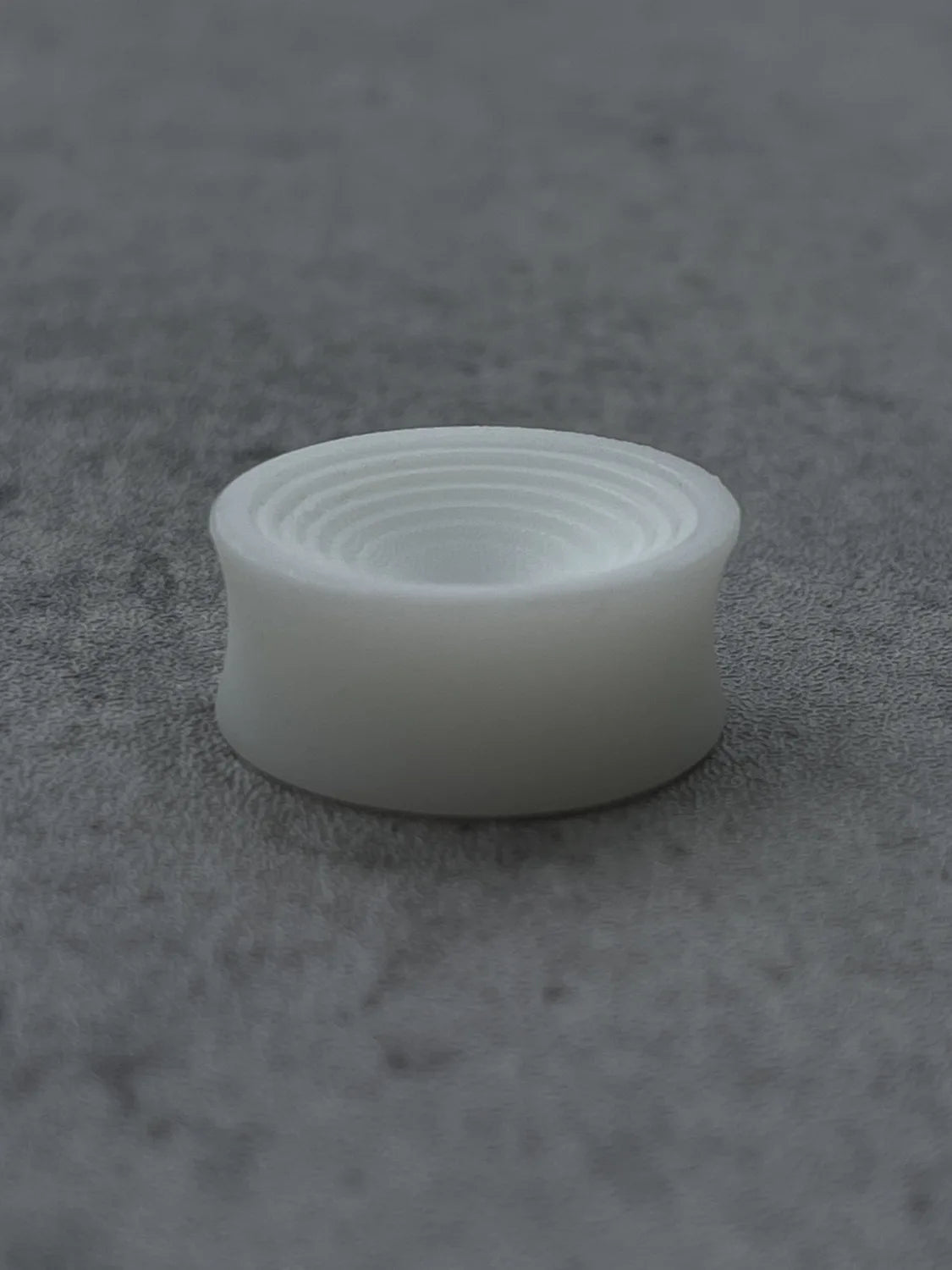 Single white Ripple double flared ear plug on a darker gray surface