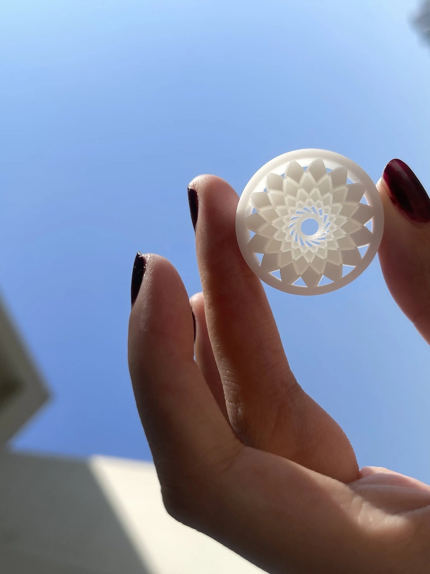 Hand holding a white Mandala double flared ear tunnel against a blue sky