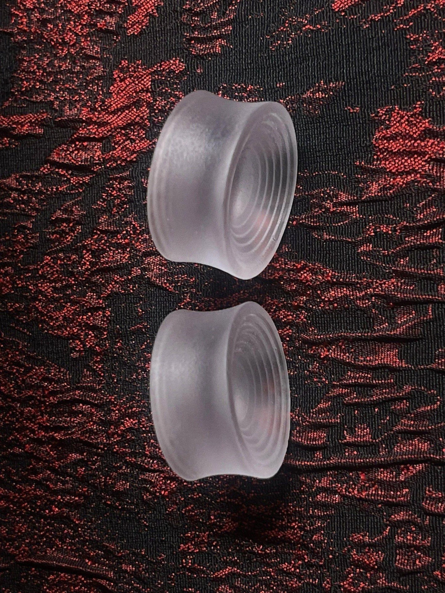 Pair of translucent Ripple double flared ear plugs on a red and black textured background