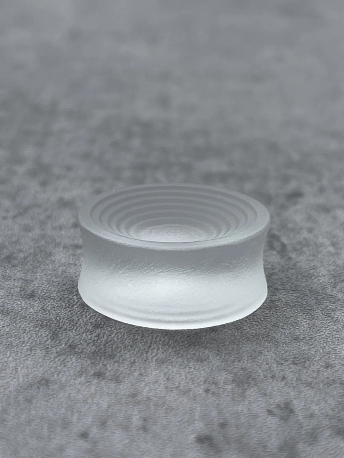 Single translucent Ripple double flared ear plug on a gray surface