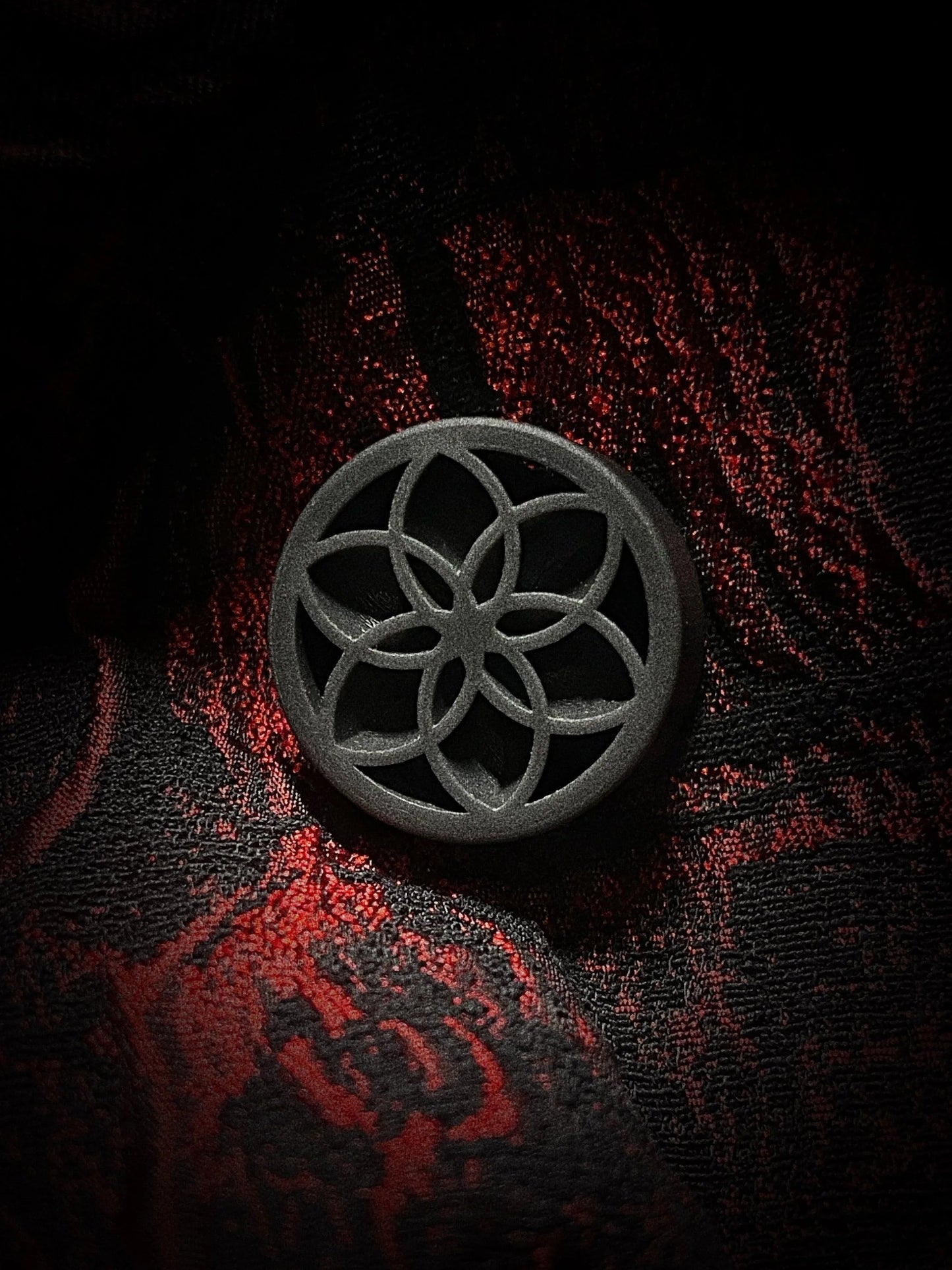 Single black Lotus double flared ear plug on a red and black textured background