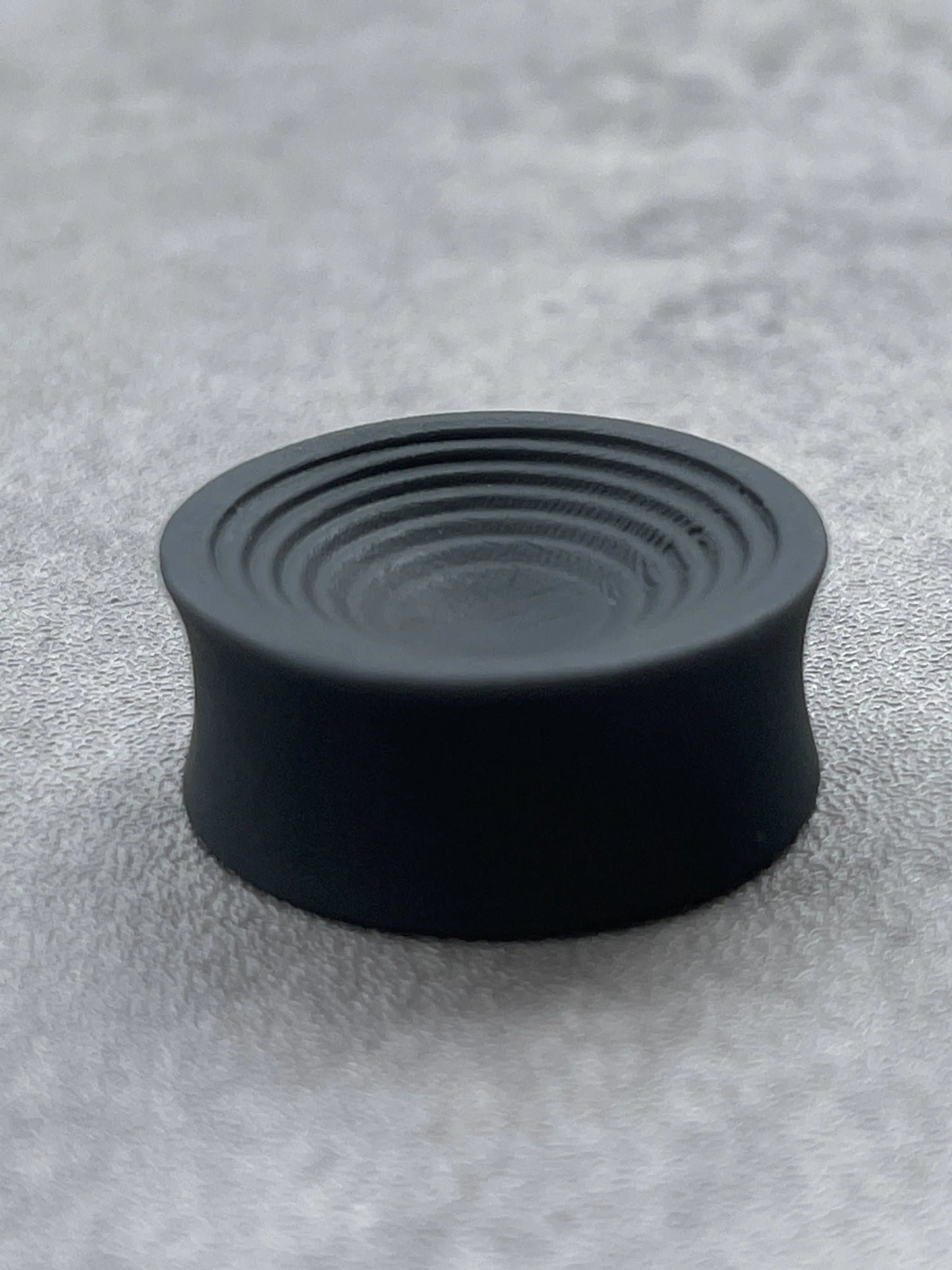 Single black Ripple double flared ear plug on a gray surface