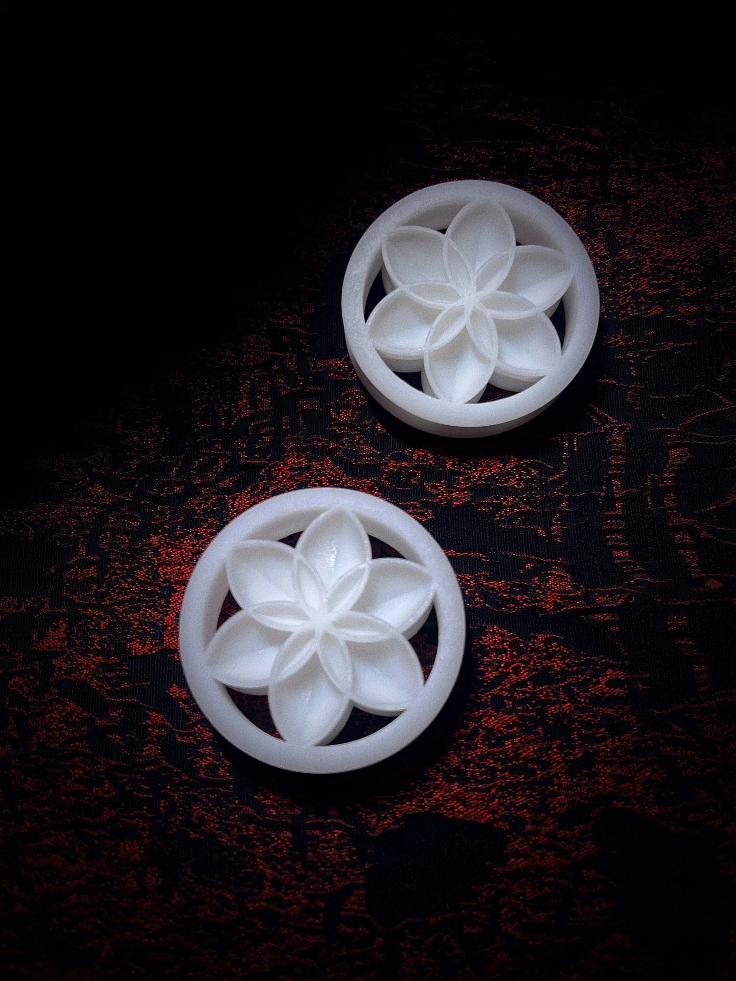 Pair of white Lotus double flared ear plugs on a red and black textured background