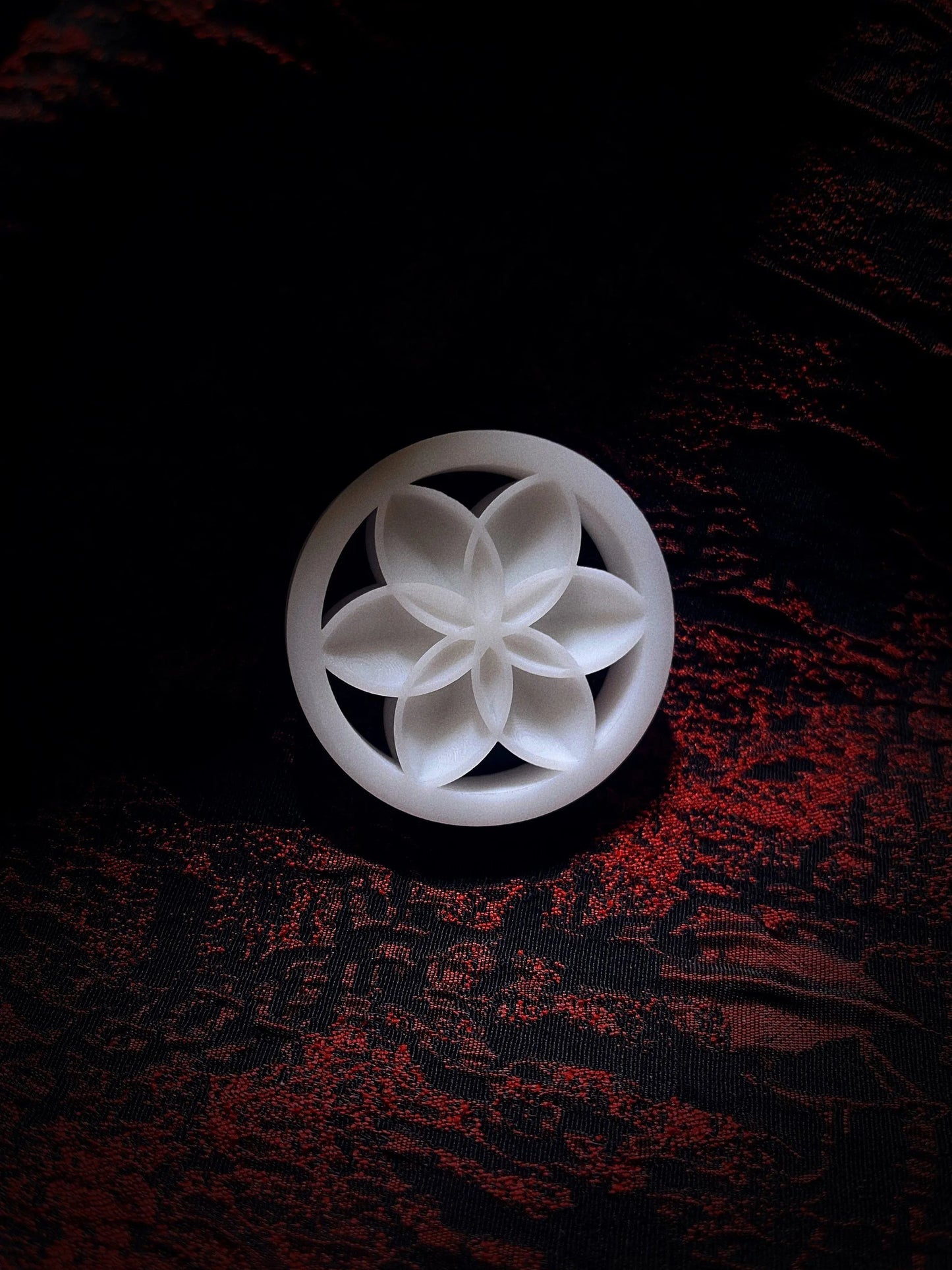 Single white Lotus double flared ear plug on a red and black textured background