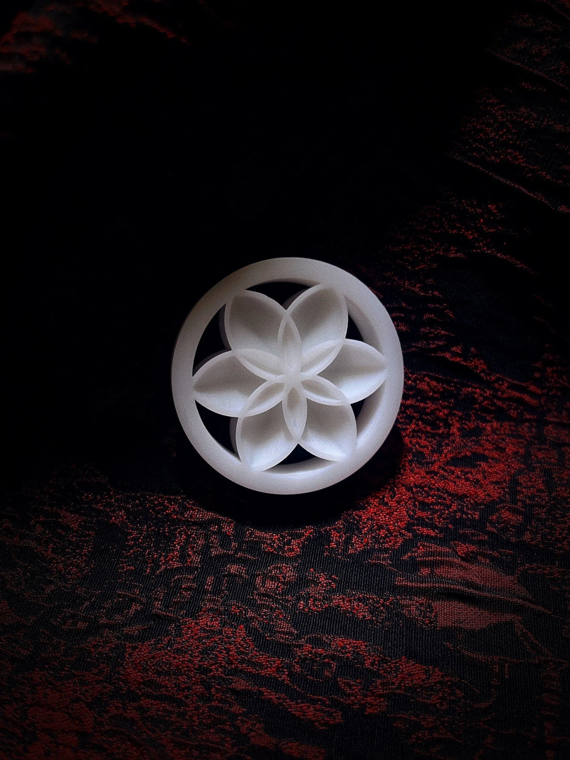 Single white Lotus double flared ear plug on a red and black textured background